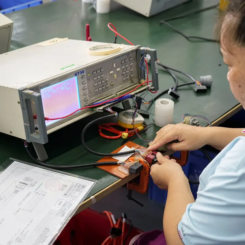 Factory worker performing 4-step quality inspection and continuity testing on a J1939 cable using a professional harness tester.